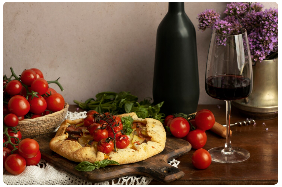 Copa de vino tinto servida junto a una pizza casera con tomates frescos y verduras, ejemplo de maridaje mediterráneo.